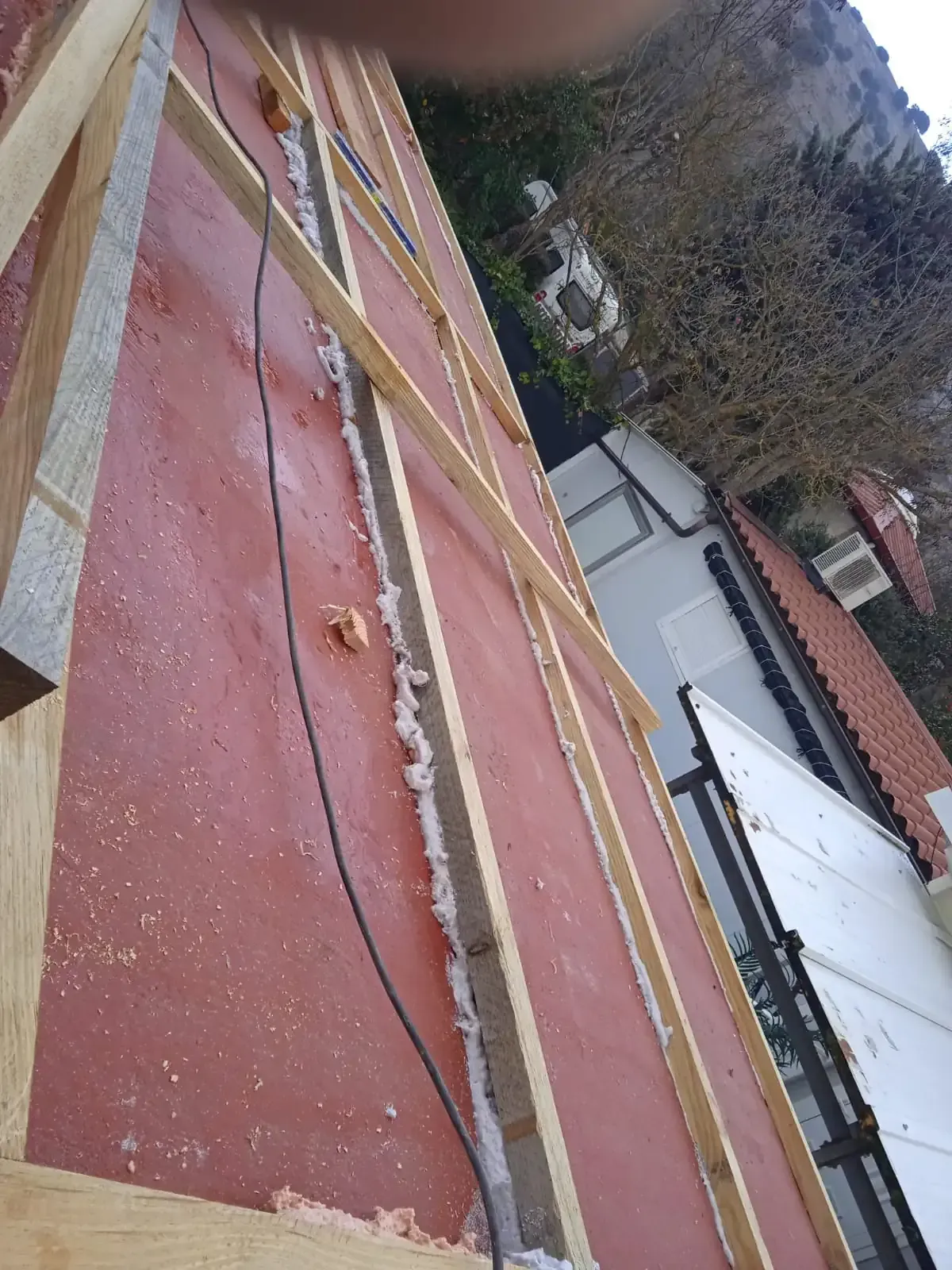 Azotea con impermeabilización roja, líneas amarillas y un cable negro junto a los edificios y árboles vecinos.