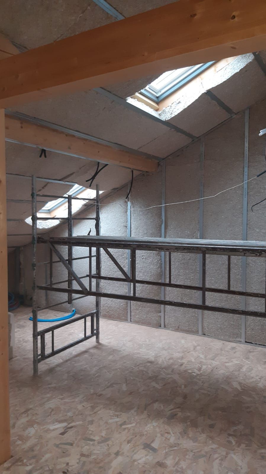 Intérieur d'une pièce en construction avec échafaudages, puits de lumière et isolation apparente.
