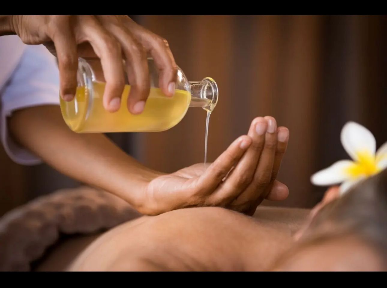 Una terapeuta realiza un masaje de espalda a un cliente que yace en una camilla de masaje en una habitación luminosa.