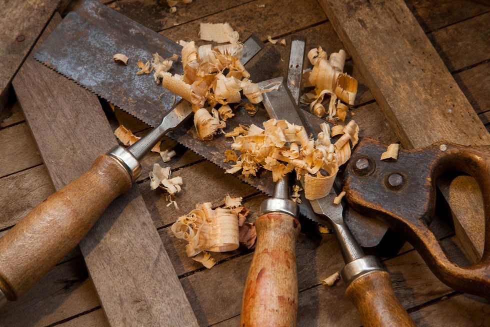 Auf einem Holztisch liegen ein Paar Meißel und eine Säge.