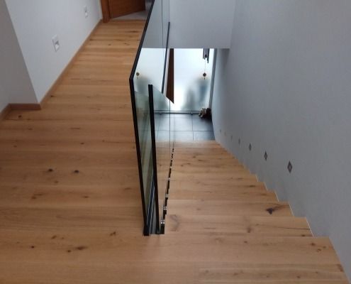 Eine Holztreppe mit einem Glasgeländer in einem Flur.