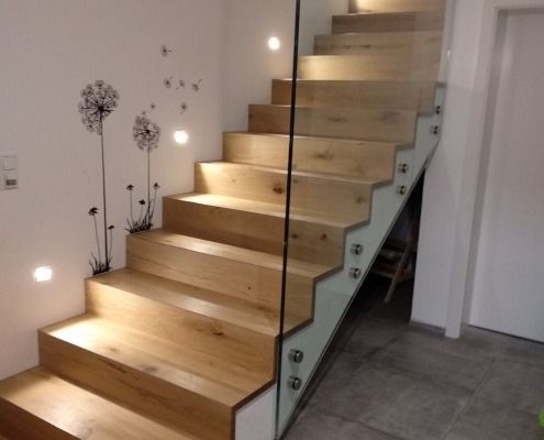 Eine Holztreppe mit Glasgeländer und Löwenzahn an der Wand