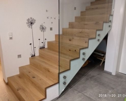 Eine Holztreppe mit Glasgeländer und Löwenzahn an der Wand