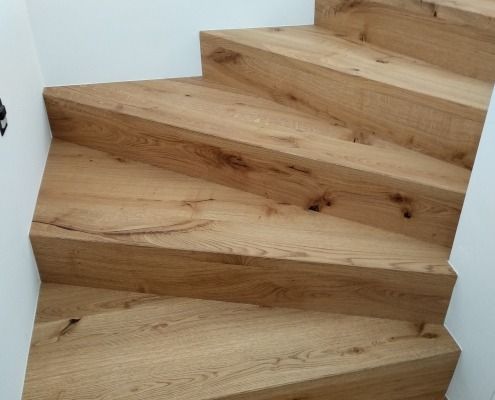 Eine Nahaufnahme einer Holztreppe mit einer weißen Wand im Hintergrund.