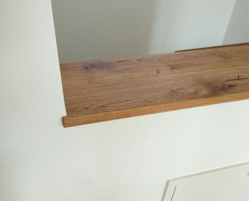 An einer weißen Wand neben einem Fenster steht ein Holzregal.