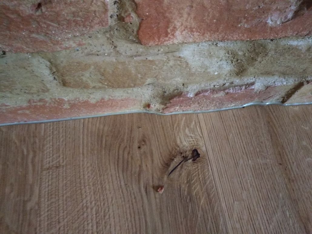 Eine Nahaufnahme eines Holzbodens neben einer Ziegelwand.