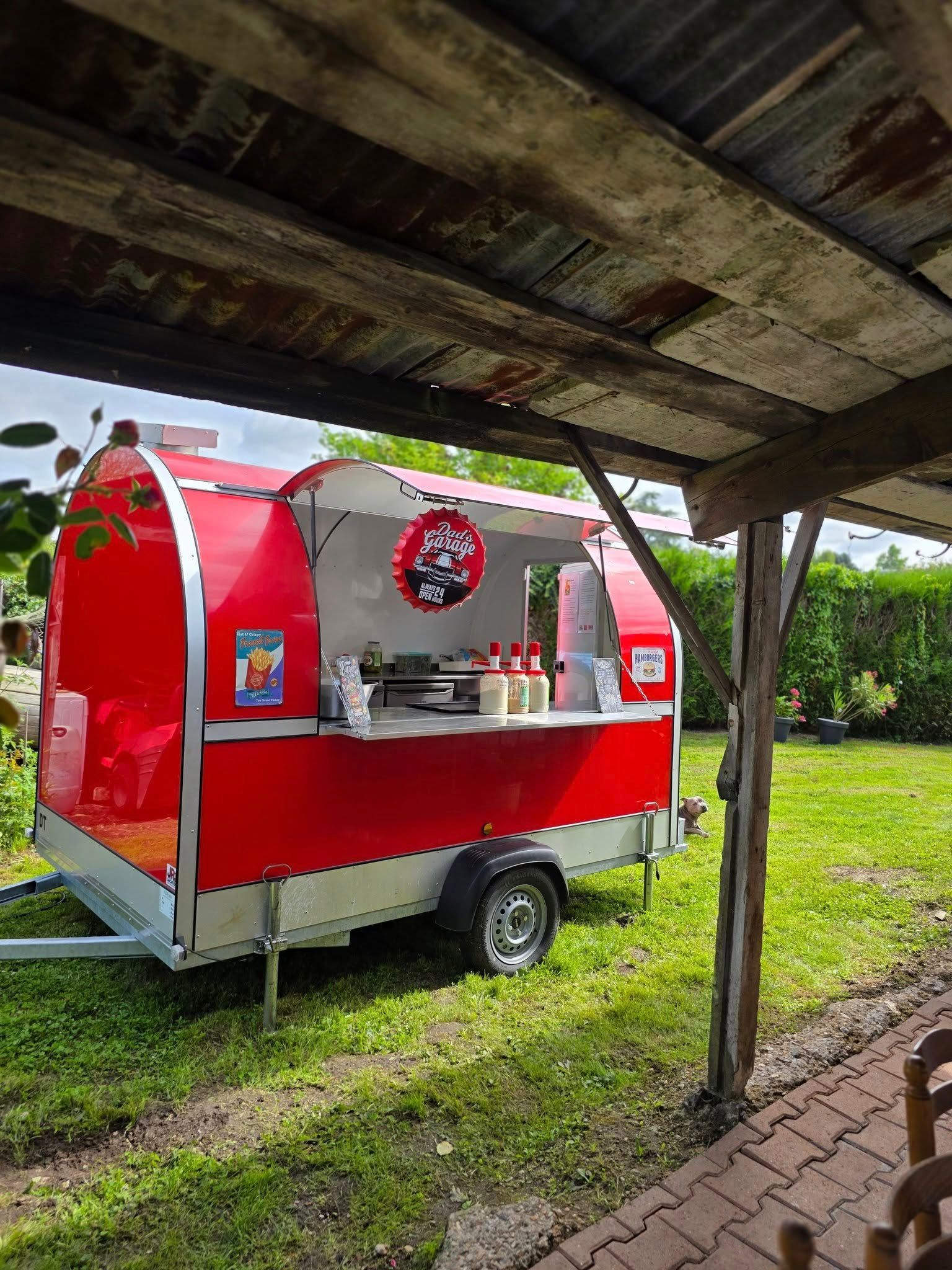 Le food truck de DALONA BURGER installée dans un jardin à côté d'un auvent en bois.