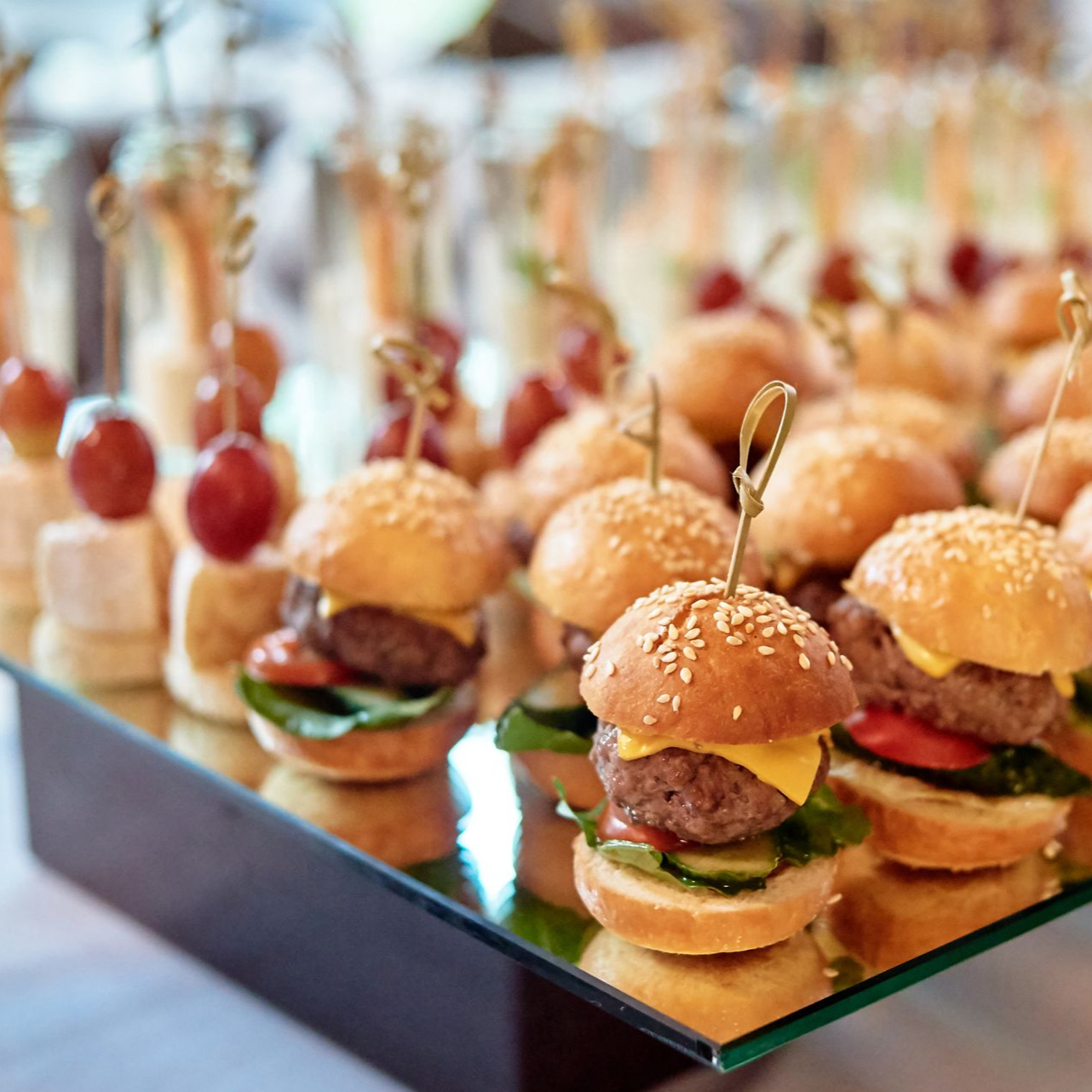 Miniburgers et amuse-gueules présentés sur un plateau, disposés pour un service traiteur.