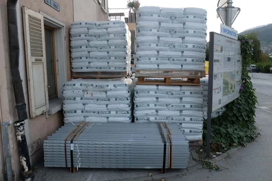 Des piles de matériaux ensachés sur des palettes en bois à côté d'un bâtiment