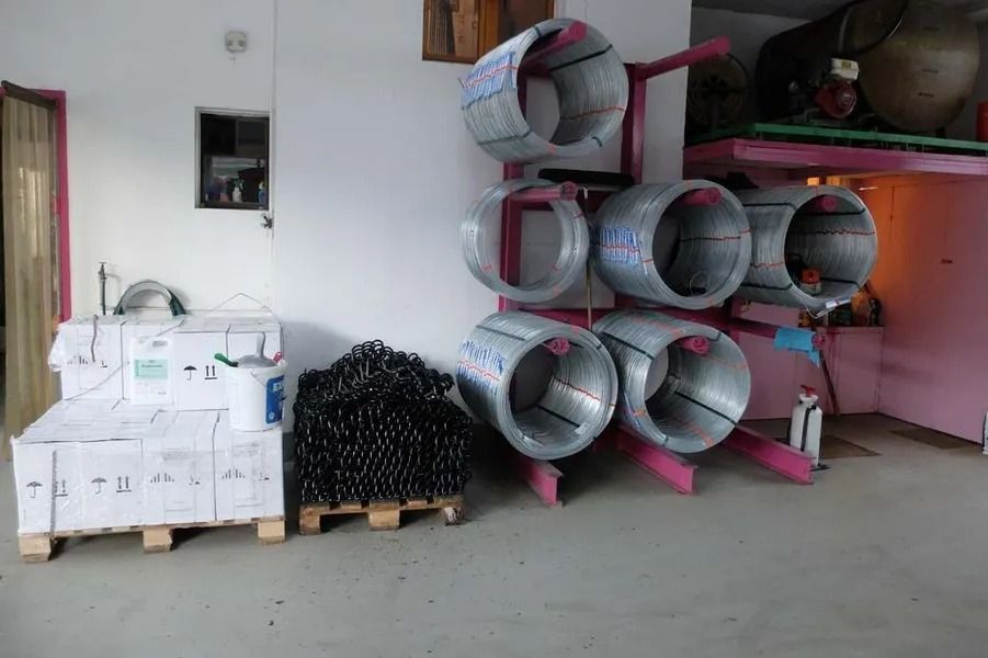 Zone de stockage avec des cartons empilés et des rangées de tuyaux métalliques sur des palettes dans une pièce ressemblant à un garage