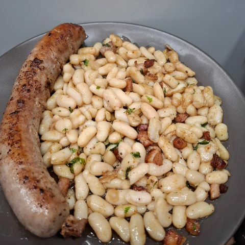 Un plato de frijoles y una salchicha en una mesa.