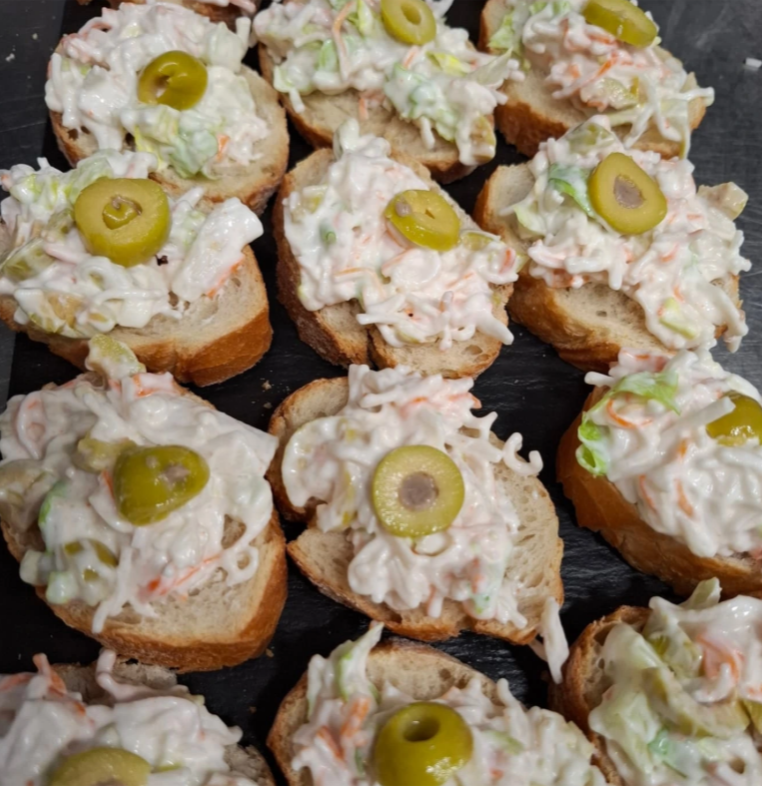 Un montón de sándwiches con ensalada de col y aceitunas encima.