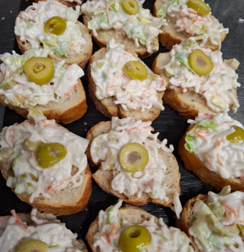Un montón de sándwiches con ensalada de col y aceitunas encima.