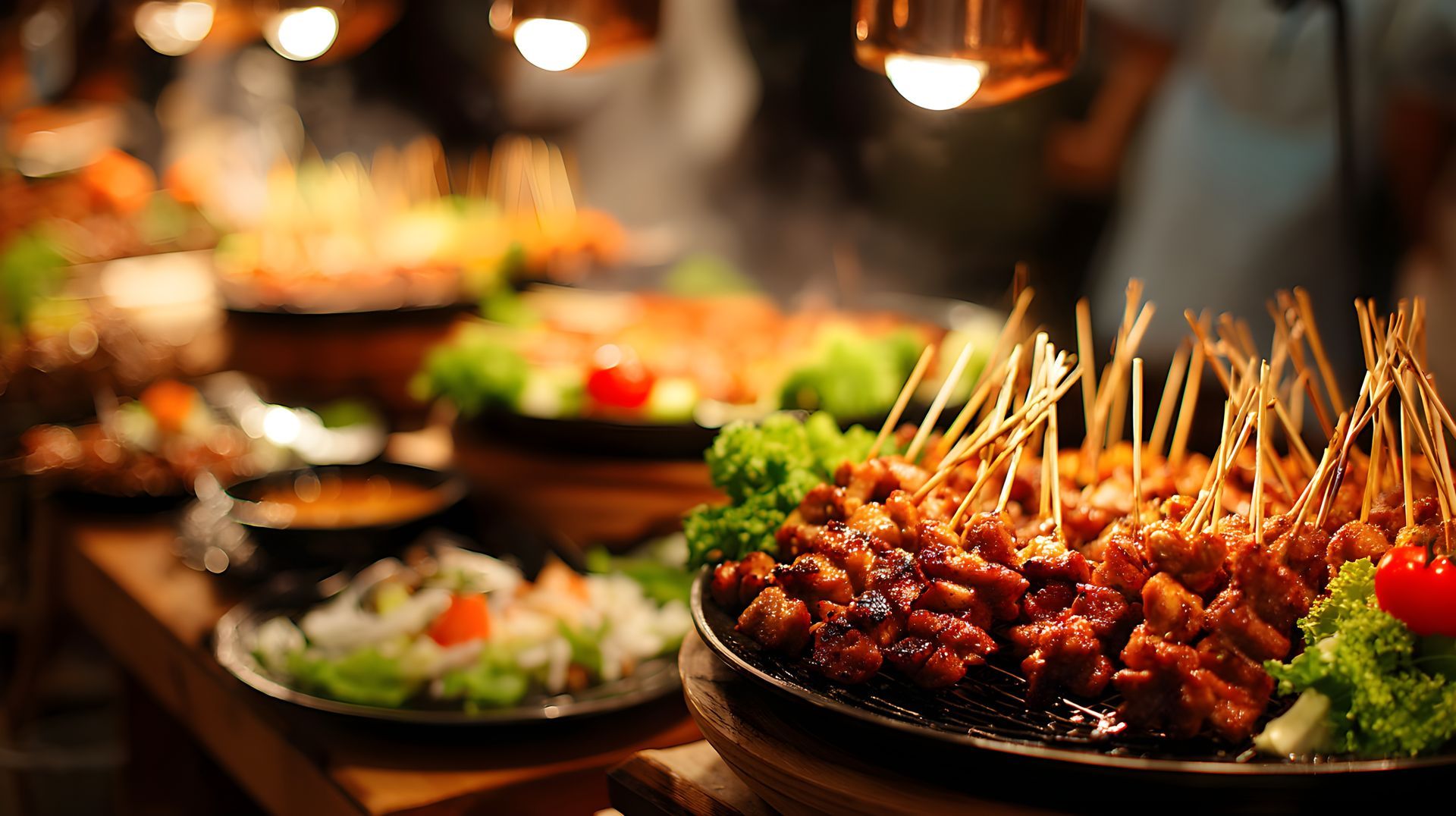 Buffet avec brochettes de viande, salade et sauces, sous un éclairage chaleureux.