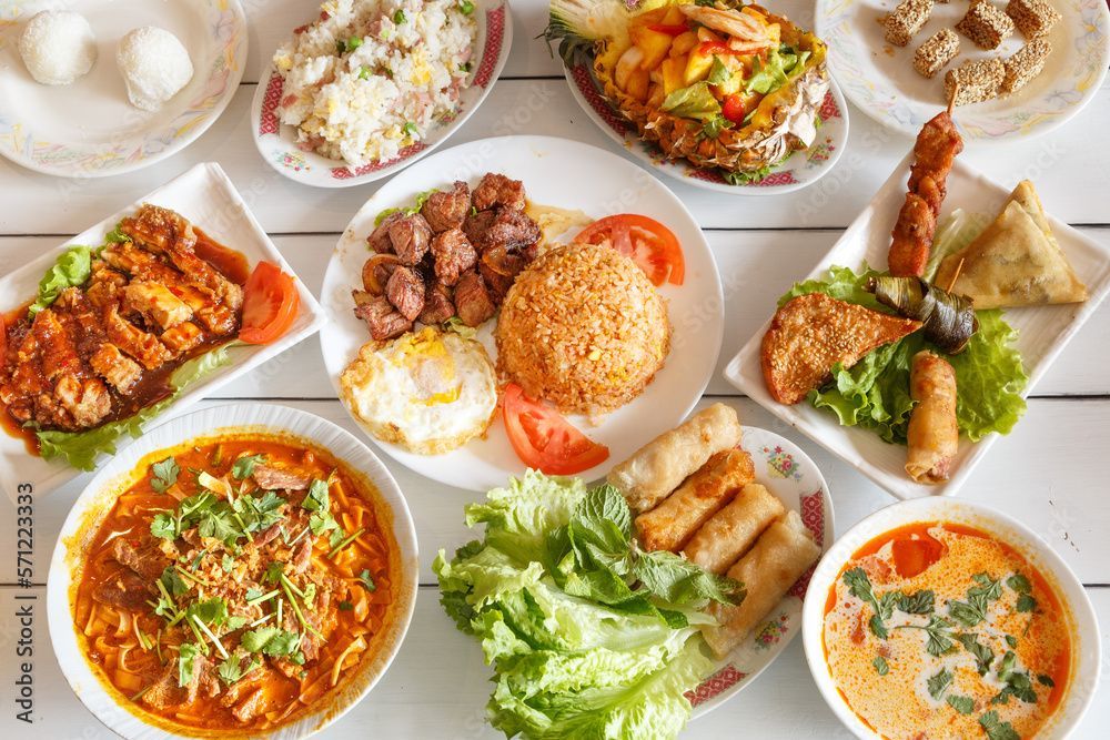 Assortiment de plats variés, comprenant soupes, riz, fritures et rouleaux de printemps, sur une surface blanche.