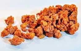 Un montón de trozos de pollo frito sobre una superficie blanca.
