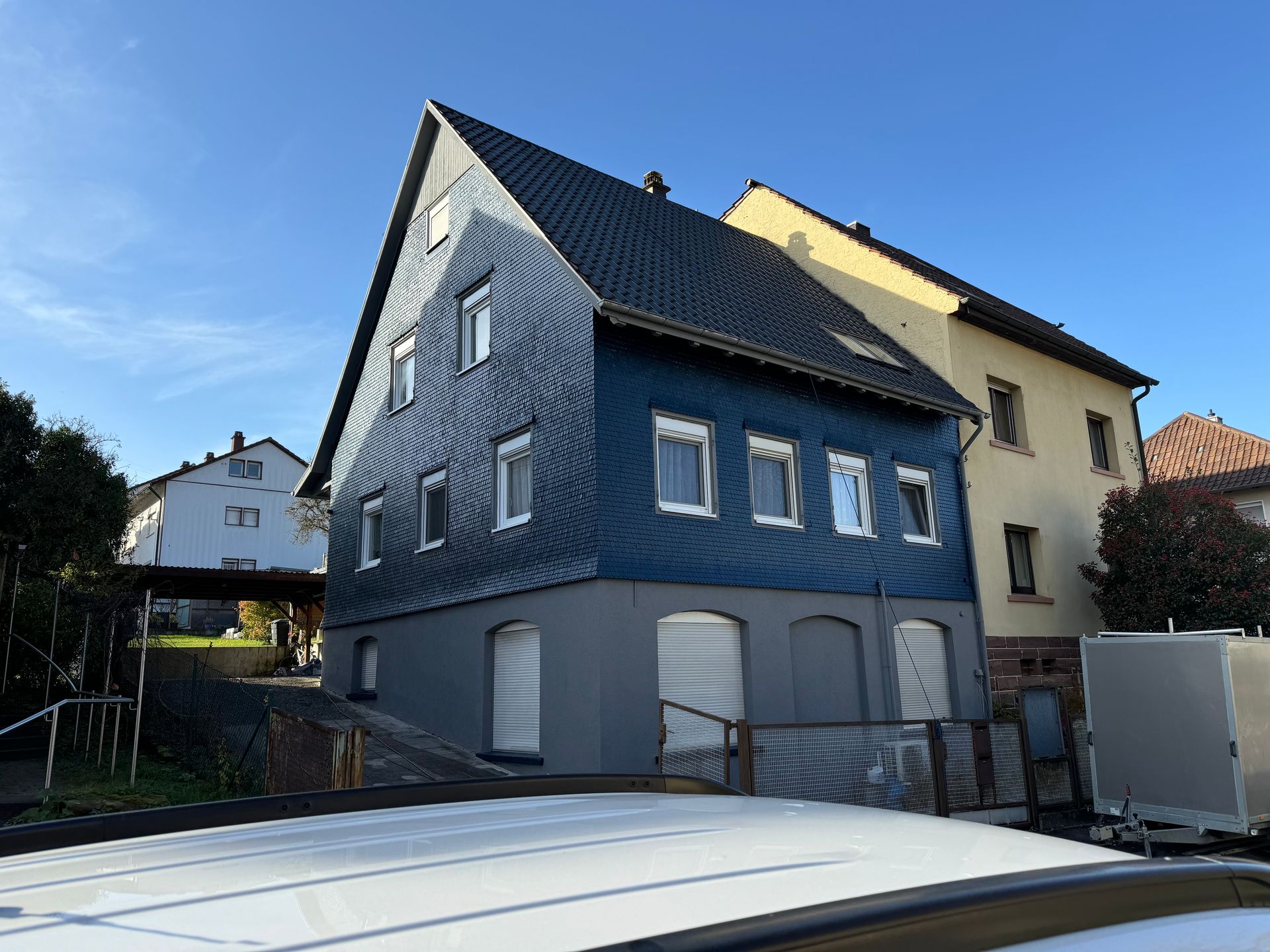 Ein blaues Gebäude mit schwarzem Dach steht neben einem weißen Gebäude