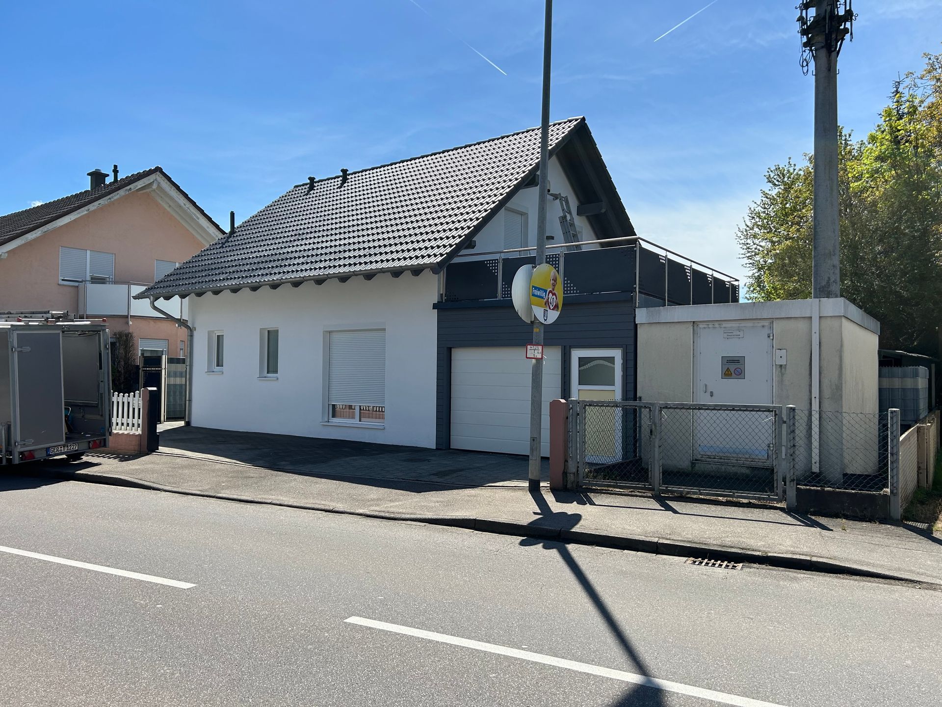 Am Straßenrand steht ein weißes Haus mit grauem Dach