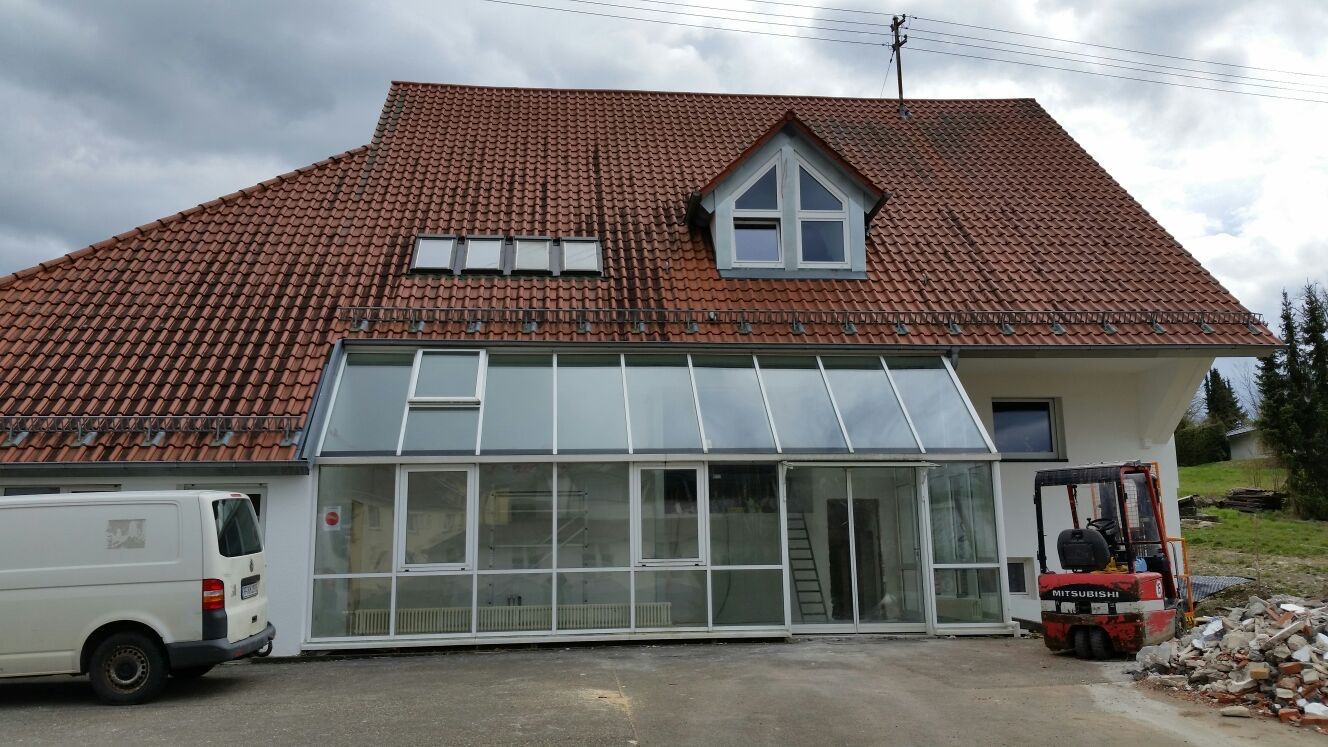 Ein weißer Lieferwagen parkt vor einem großen Haus mit Wintergarten