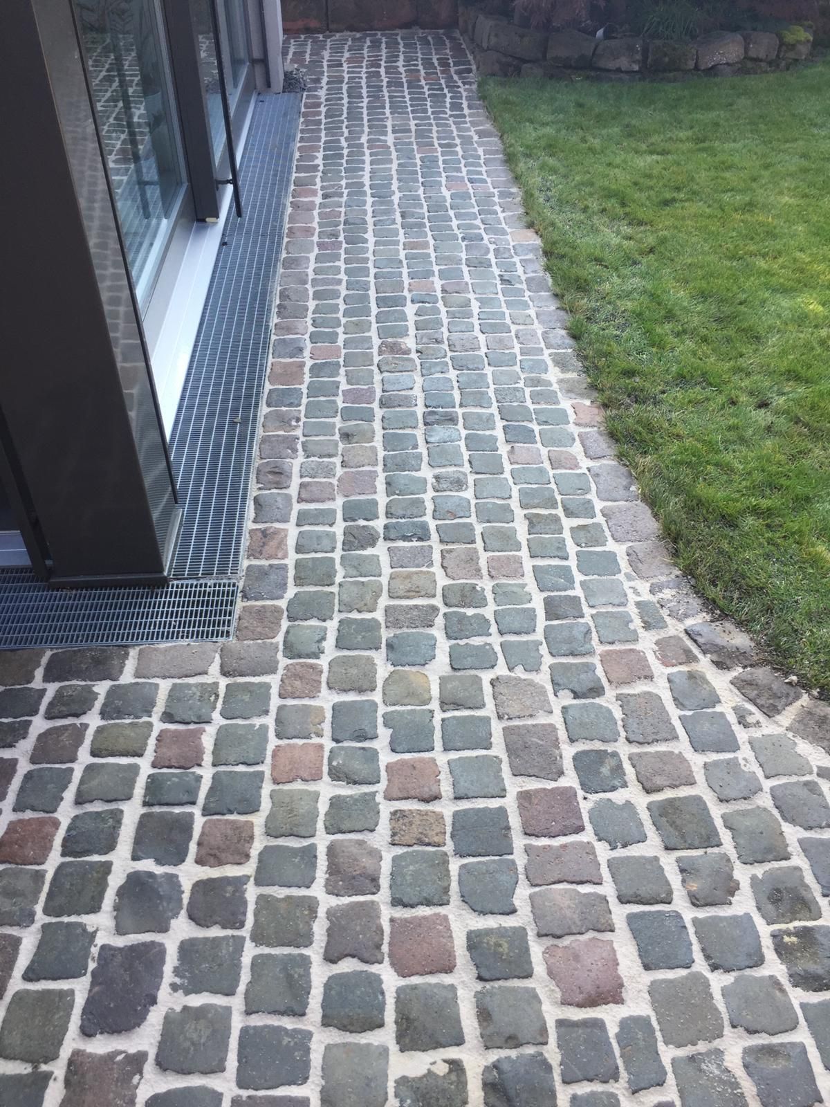 Ein Kopfsteinpflasterweg führt zu einem Haus, im Hintergrund ist ein Rasen zu sehen