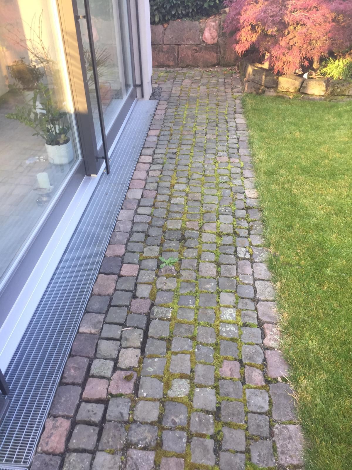 Ein gemauerter Gehweg führt zu einem Haus mit einer Glasschiebetür