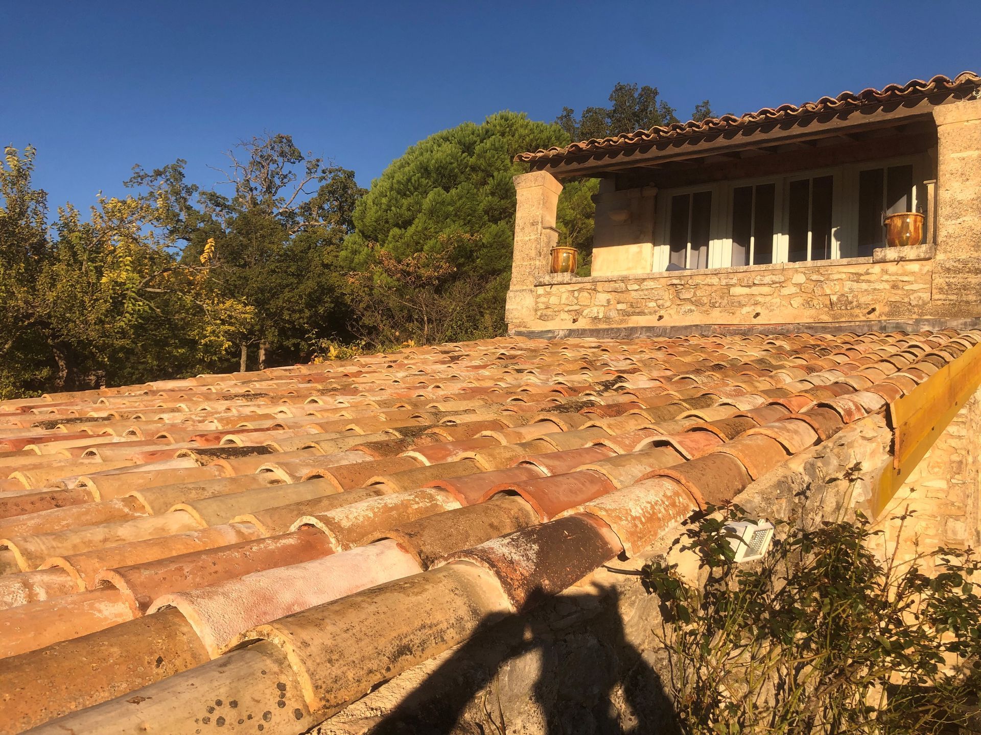 Des tuiles de terre cuite baignées de soleil mènent à une maison rustique en pierre avec un petit balcon sous un ciel bleu.