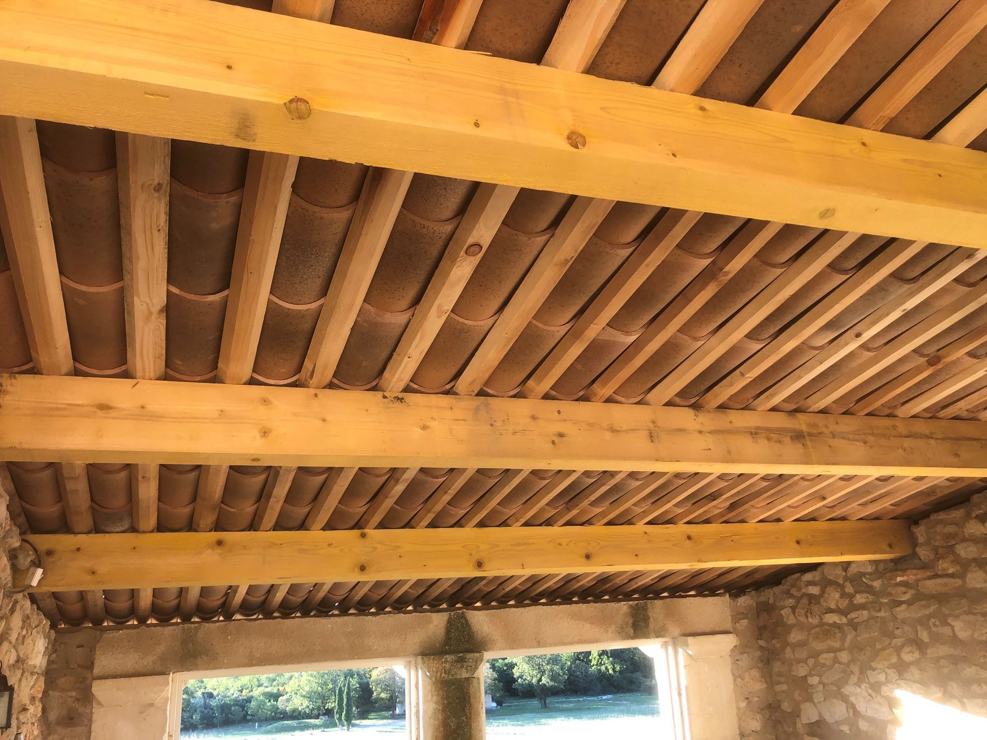Plafond à poutres apparentes sous une structure rustique en pierre avec chevrons apparents et fenêtres en dessous