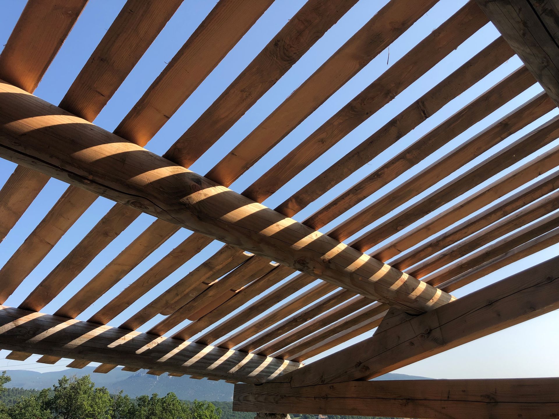 Lattes d'une pergola en bois se détachant sur un ciel bleu au-dessus d'un paysage désertique