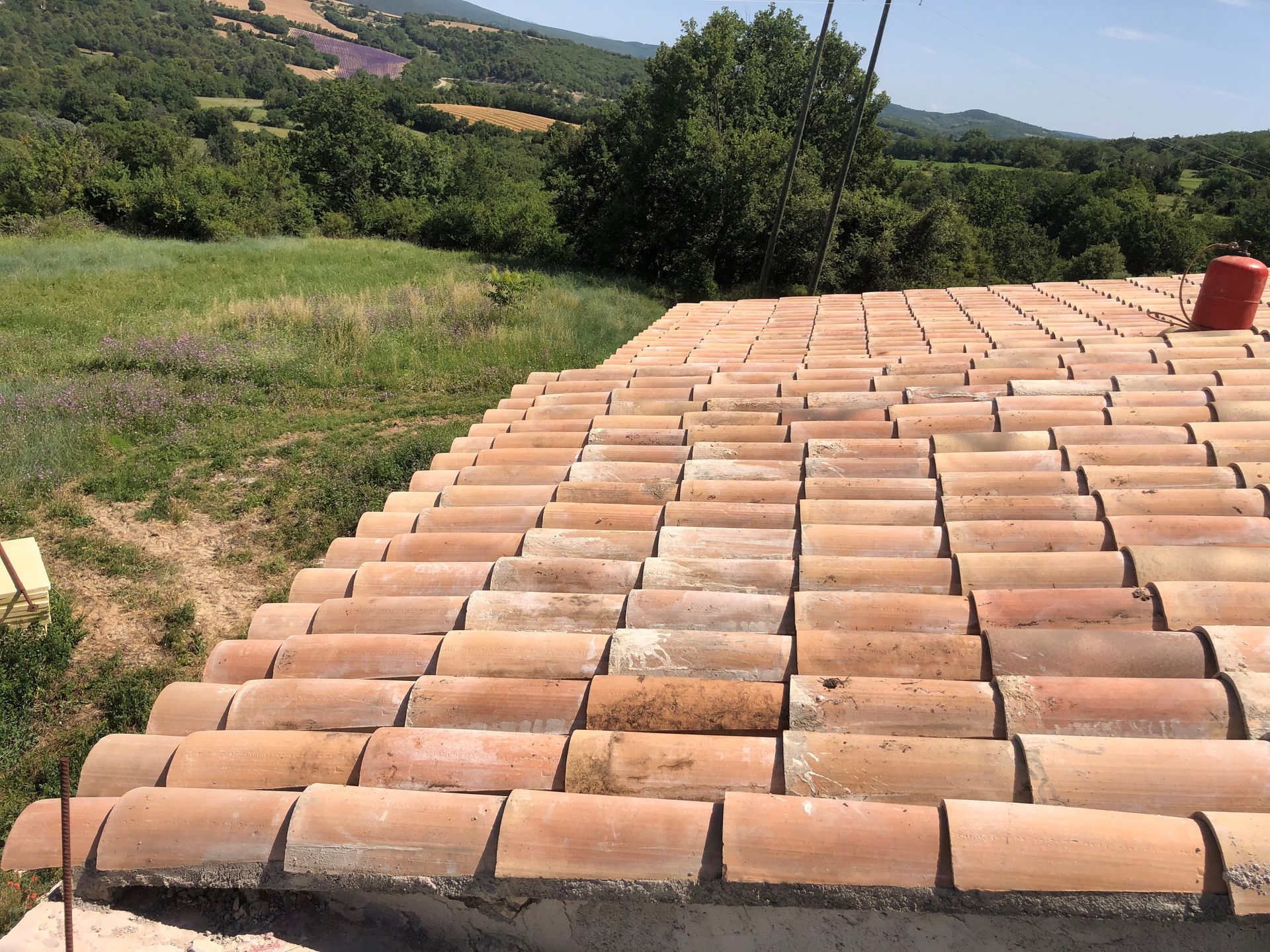 Toit de tuiles en terre cuite donnant sur des champs verdoyants et des arbres sous un ciel ensoleillé