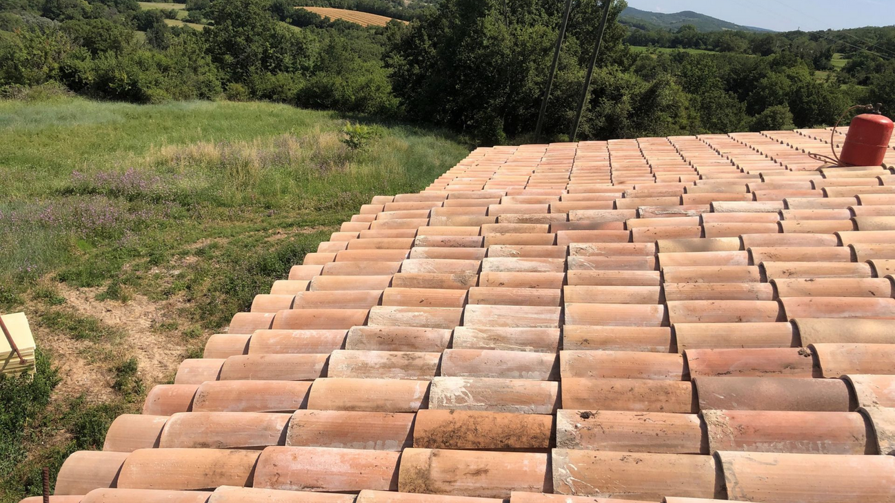 Toiture en tuiles de terre cuite, campagne verdoyante et collines en arrière-plan