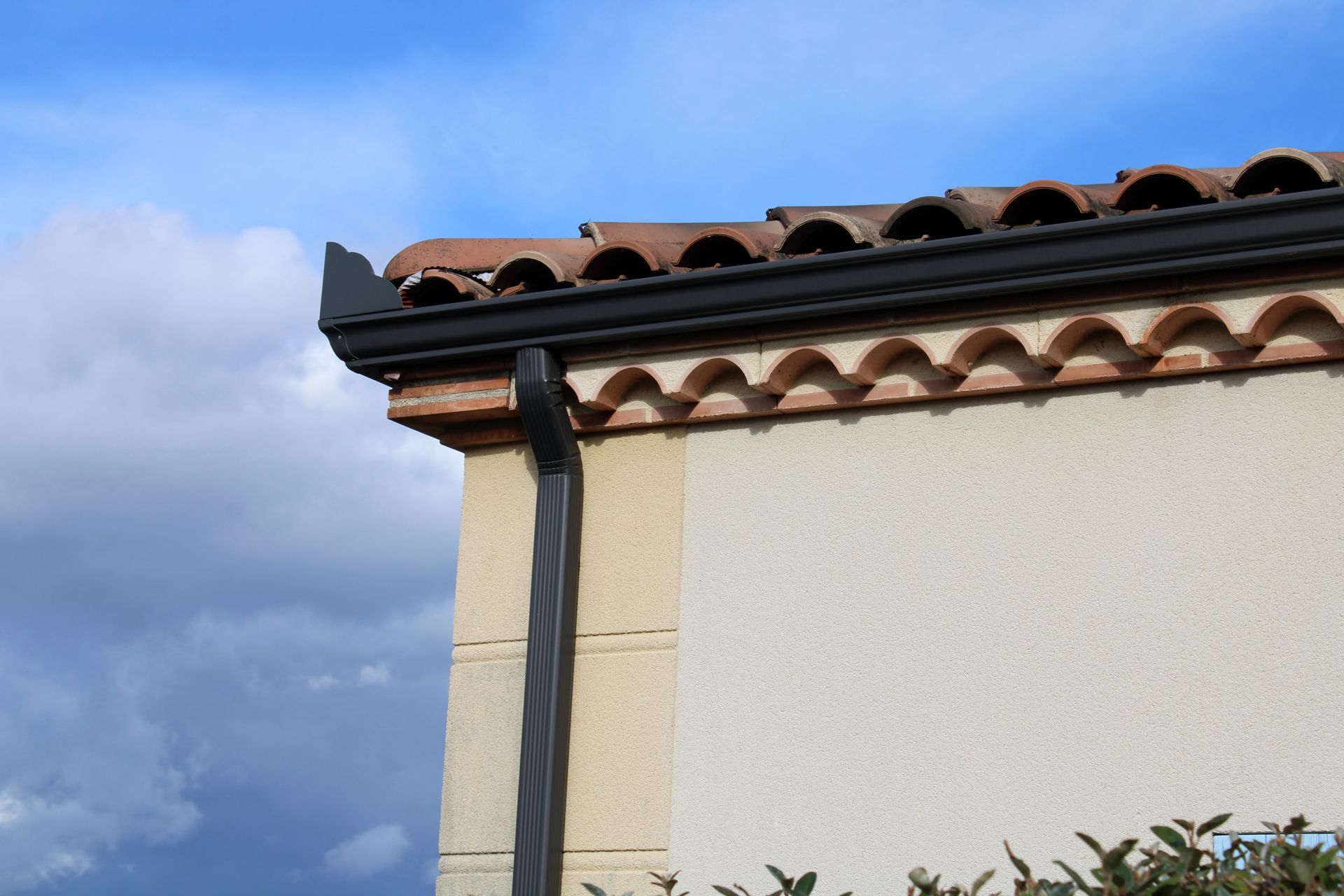 Coin d'un bâtiment en stuc avec un toit de tuiles en terre cuite sur un ciel bleu nuageux