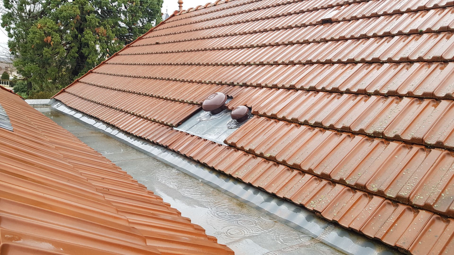 Réparation de toiture en tuiles rouges avec sous-couche apparente et un ouvrier près d'une ouverture de puits de lumière