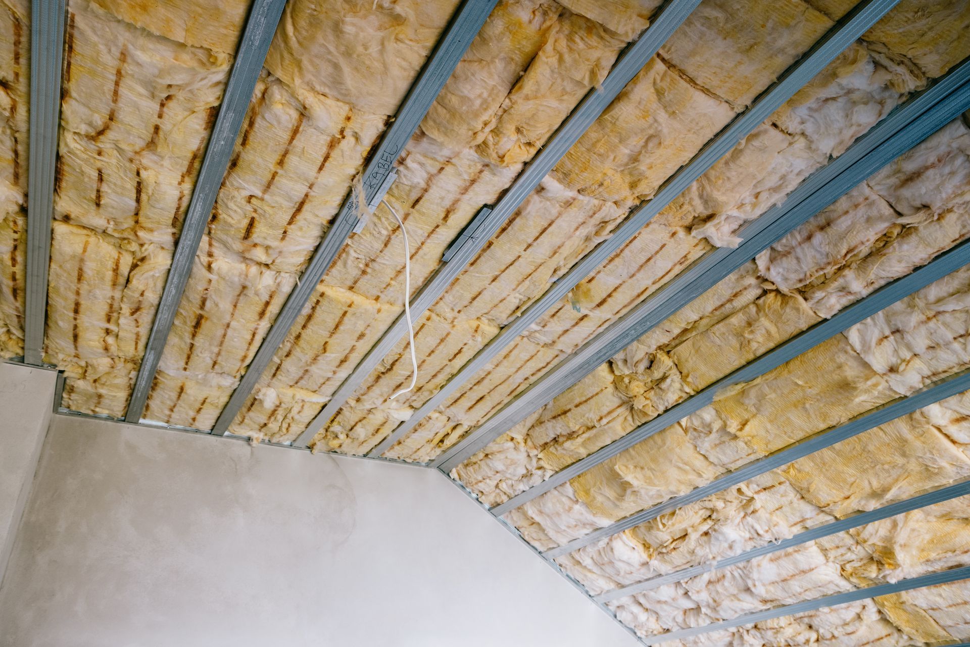 Plafond avec isolation jaune apparente et poutres de charpente bleues dans un coin de pièce