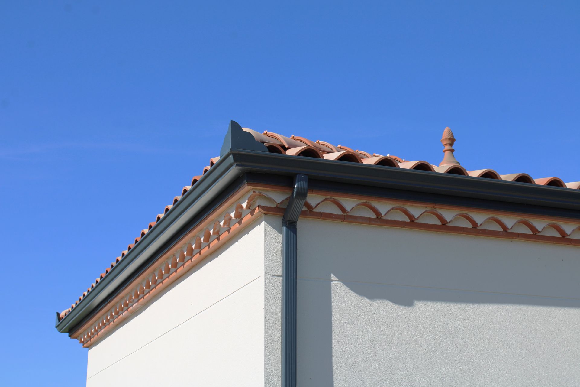 Coin d'un bâtiment en stuc blanc avec un toit de tuiles sombres se détachant sur un ciel bleu clair