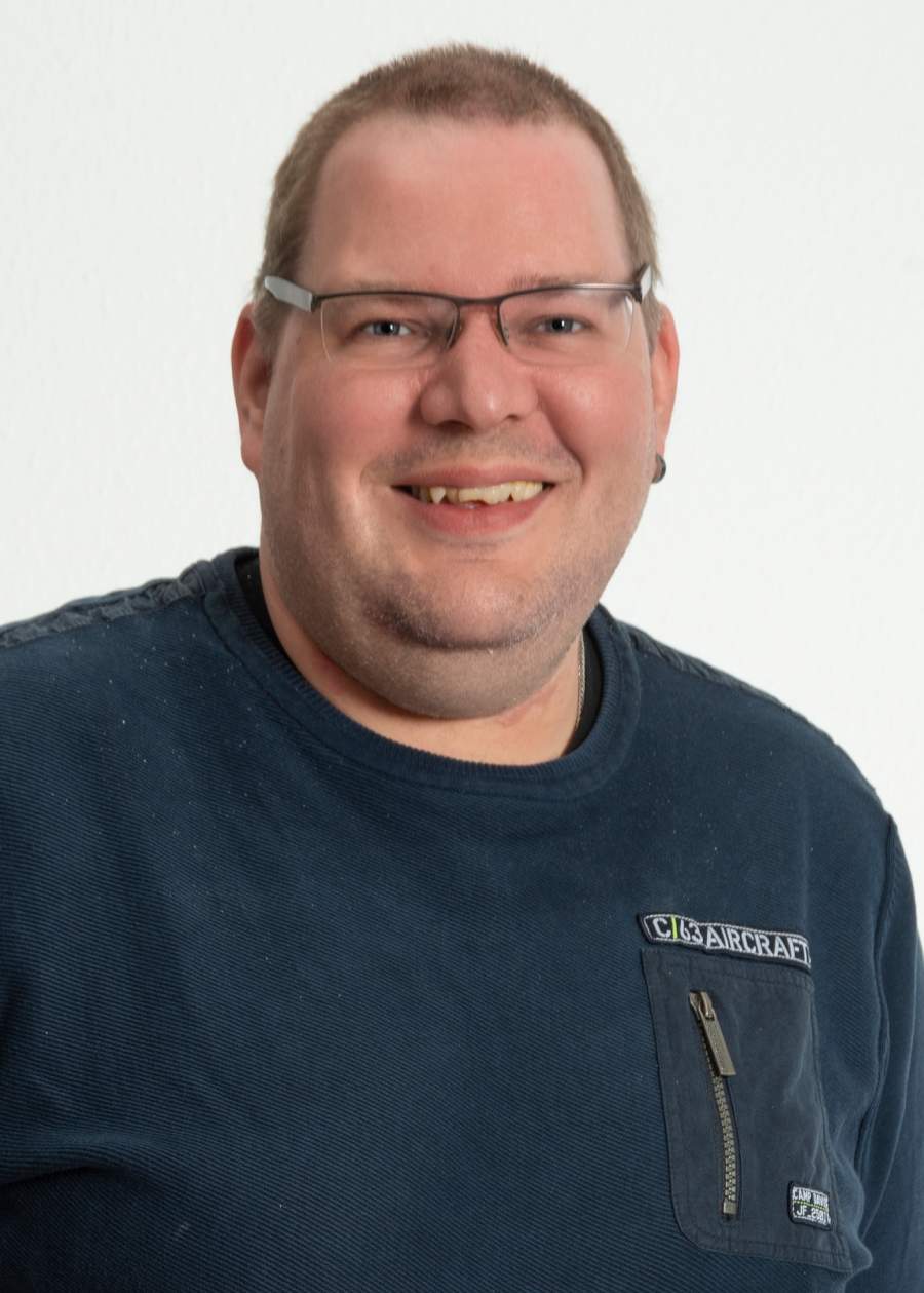 Lächelnder Mann mit Brille, blauer Pullover, vor weißem Hintergrund.