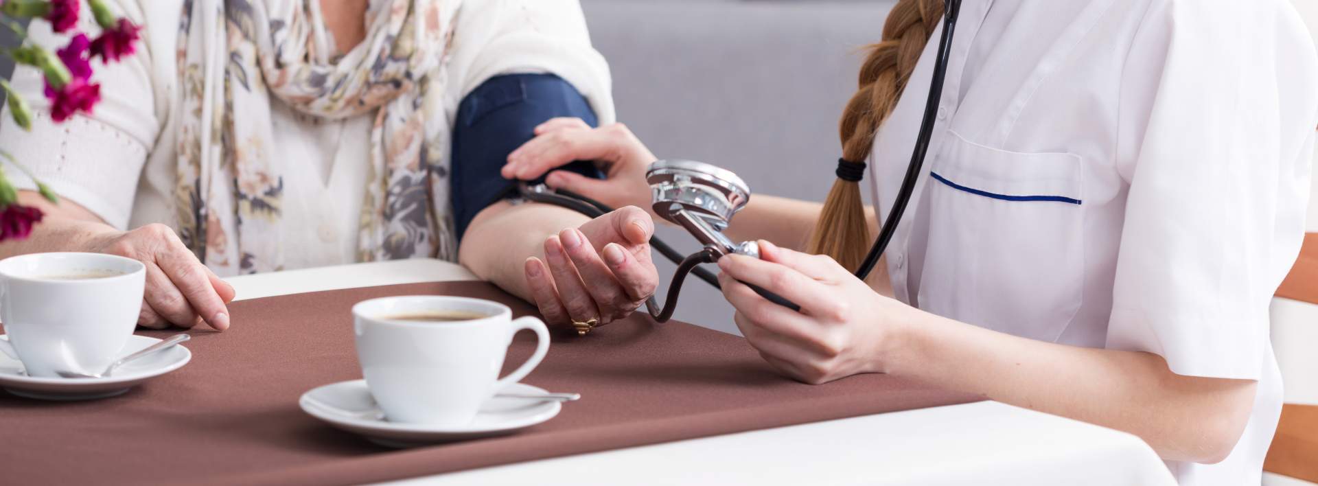 Bei einer Frau wird beim Kaffeetrinken an einem Tisch der Blutdruck gemessen; der Test wird von einem Arzt durchgeführt.