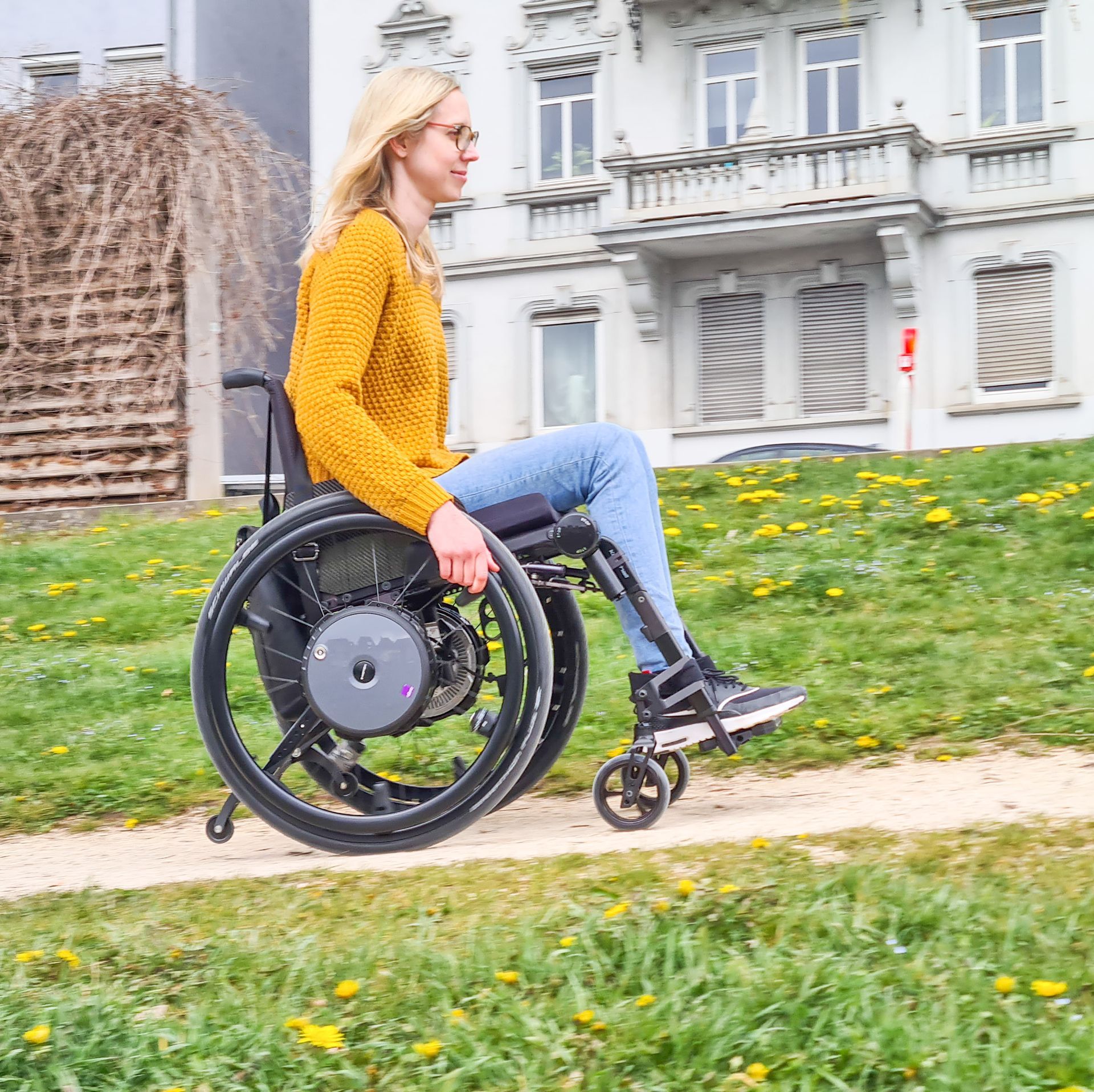 Eine Frau in einem gelben Pullover sitzt in einem Rollstuhl.