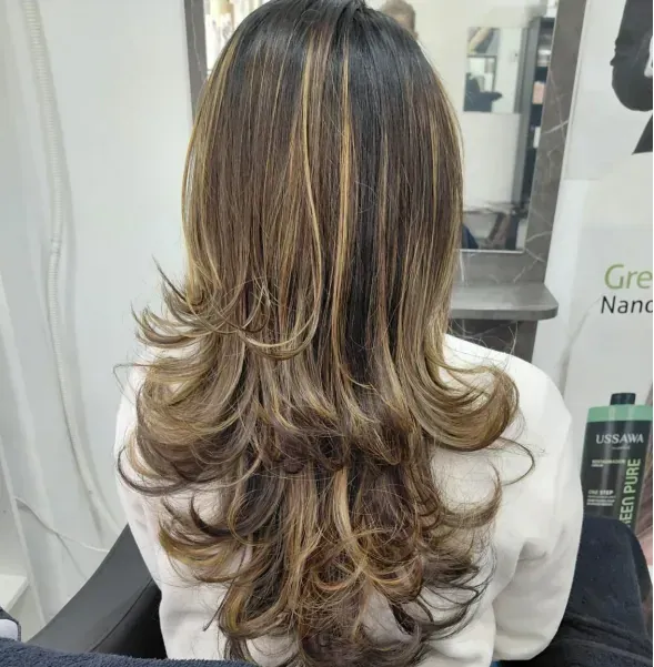 Mujer con cabello en capas y con reflejos en un salón de belleza.