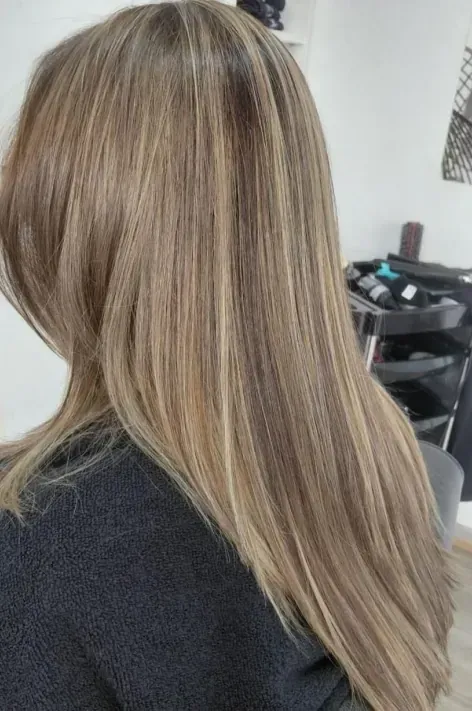 Mujer con cabello castaño claro, largo y liso con reflejos rubios, en entorno de salón.
