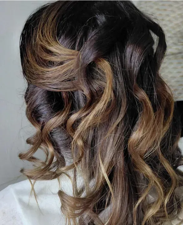 Cabello de mujer peinado con rizos semirecogidos con raíces color castaño oscuro y reflejos color caramelo.