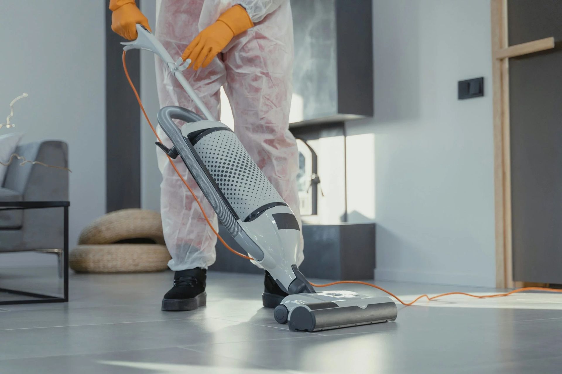 Personne passant l'aspirateur sur le sol d'un salon moderne avec un aspirateur traîneau et des gants orange