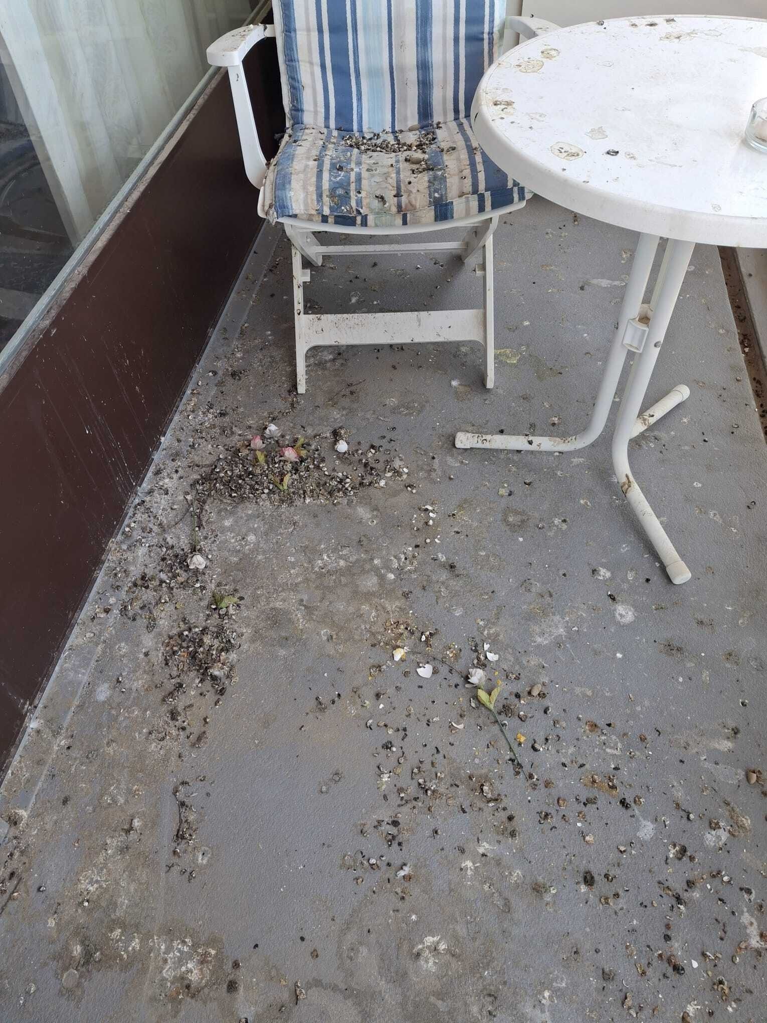 Sol de patio poussiéreux à côté d'une chaise à rayures et d'une petite table ronde blanche, avec des débris éparpillés.