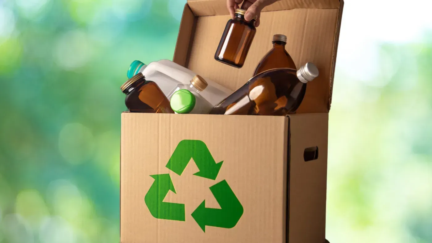 Una persona está colocando una botella en una caja de reciclaje.