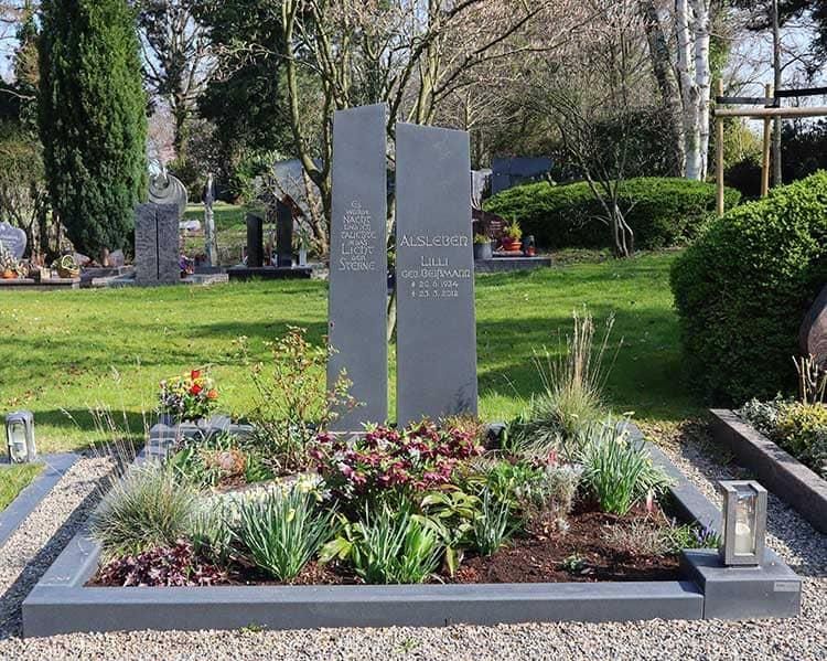 Ein Grab auf einem Friedhof, umgeben von Blumen und Büschen
