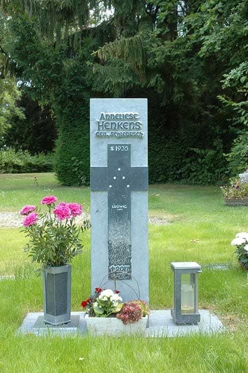 Ein Grabstein mit einem Kreuz und Blumen auf einem Friedhof.