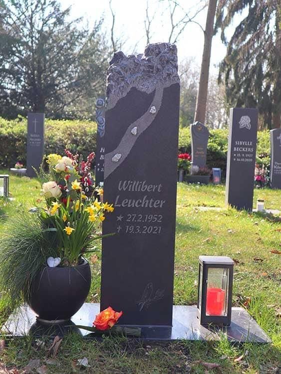 Ein Grabstein auf einem Friedhof mit einer Blumenvase und einer Laterne.