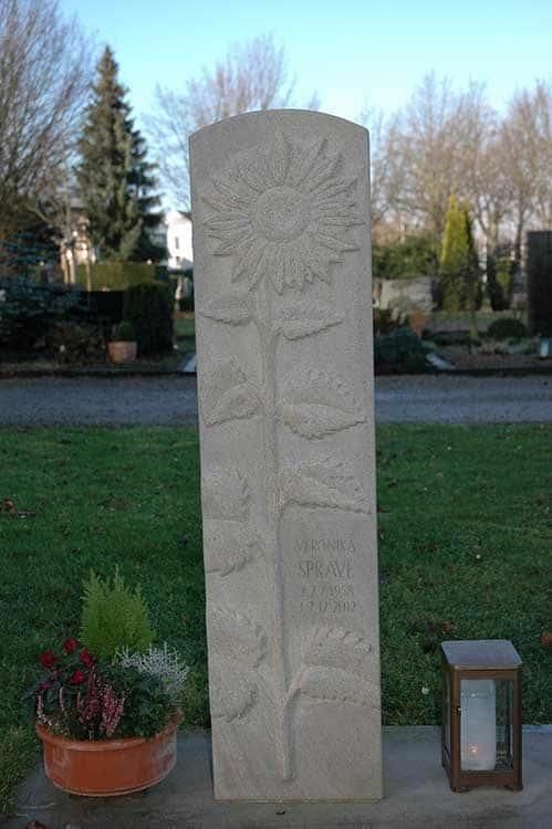 Auf einem Friedhof steht ein Grabstein mit einer eingeritzten Sonnenblume.
