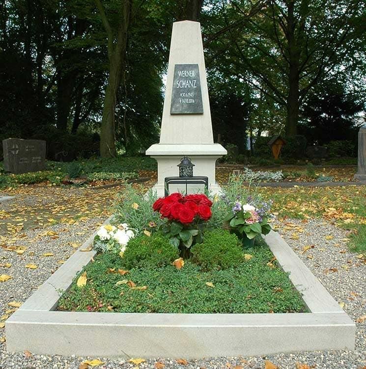 Ein Grab auf einem Friedhof mit Blumen und einer Gedenktafel