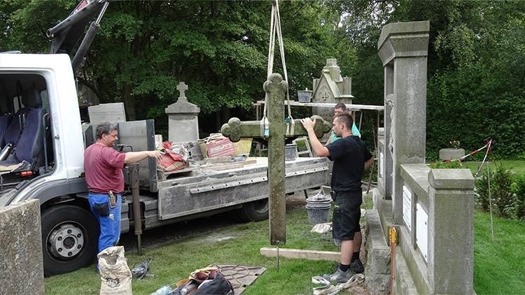 Zwei Männer arbeiten auf einem Friedhof neben einem Lastwagen an einem Kreuz.