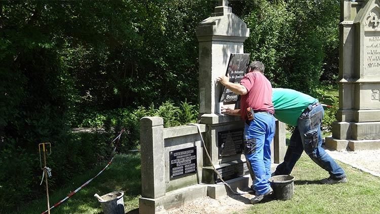 Zwei Männer arbeiten an einem Denkmal auf einem Friedhof.